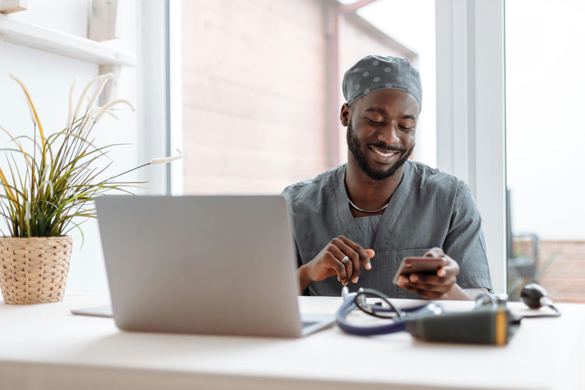 Smiling healthcare professional using phone in office with laptop and medical tools.